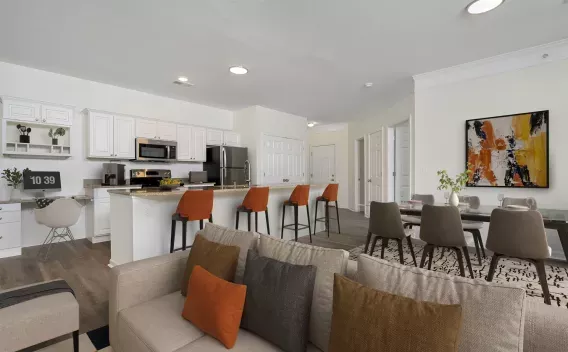 Open-concept living room, kitchen with orange bar stools, and dining area with abstract art.