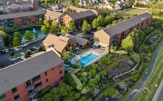 Aerial photograph: Modern apartment complex with red brick buildings, a bright blue swimming pool, a pond, and green landscaping.