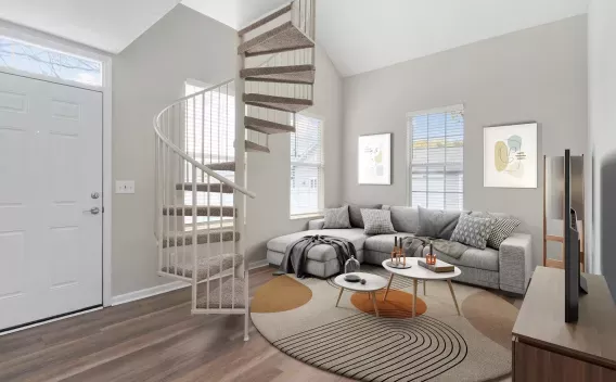 Modern living room with a white spiral staircase, gray sectional sofa, abstract art, and two round coffee tables.