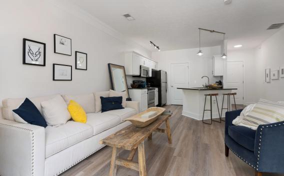Modern open-concept living room and kitchen with a cream sofa, blue armchair, and rustic wood coffee table.