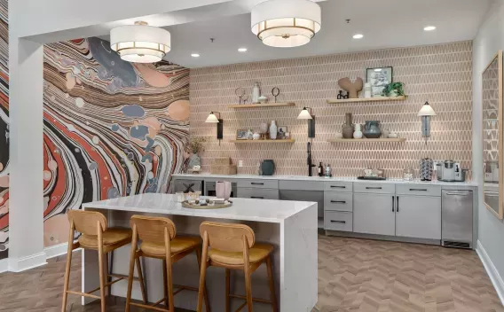 Stylish kitchen area with marble island, brown bar stools, tiled wall, and abstract art in orange, gray, and black.