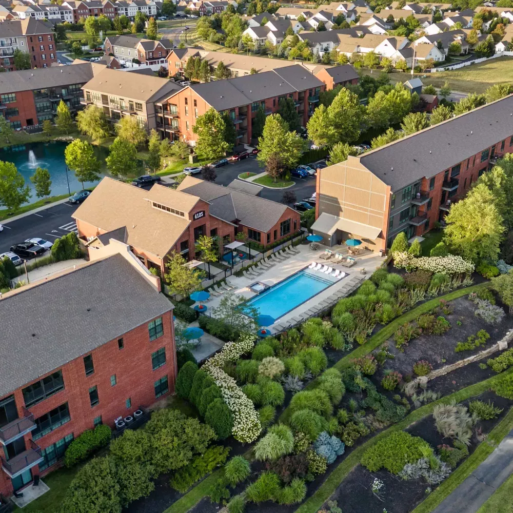 Aerial photograph: Modern apartment complex with red brick buildings, a bright blue swimming pool, a pond, and green landscaping.