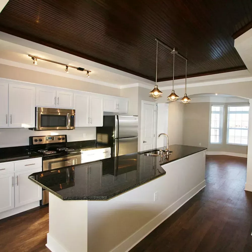 Modern kitchen with white cabinets, black granite island, stainless steel appliances, and a dark coffered ceiling.