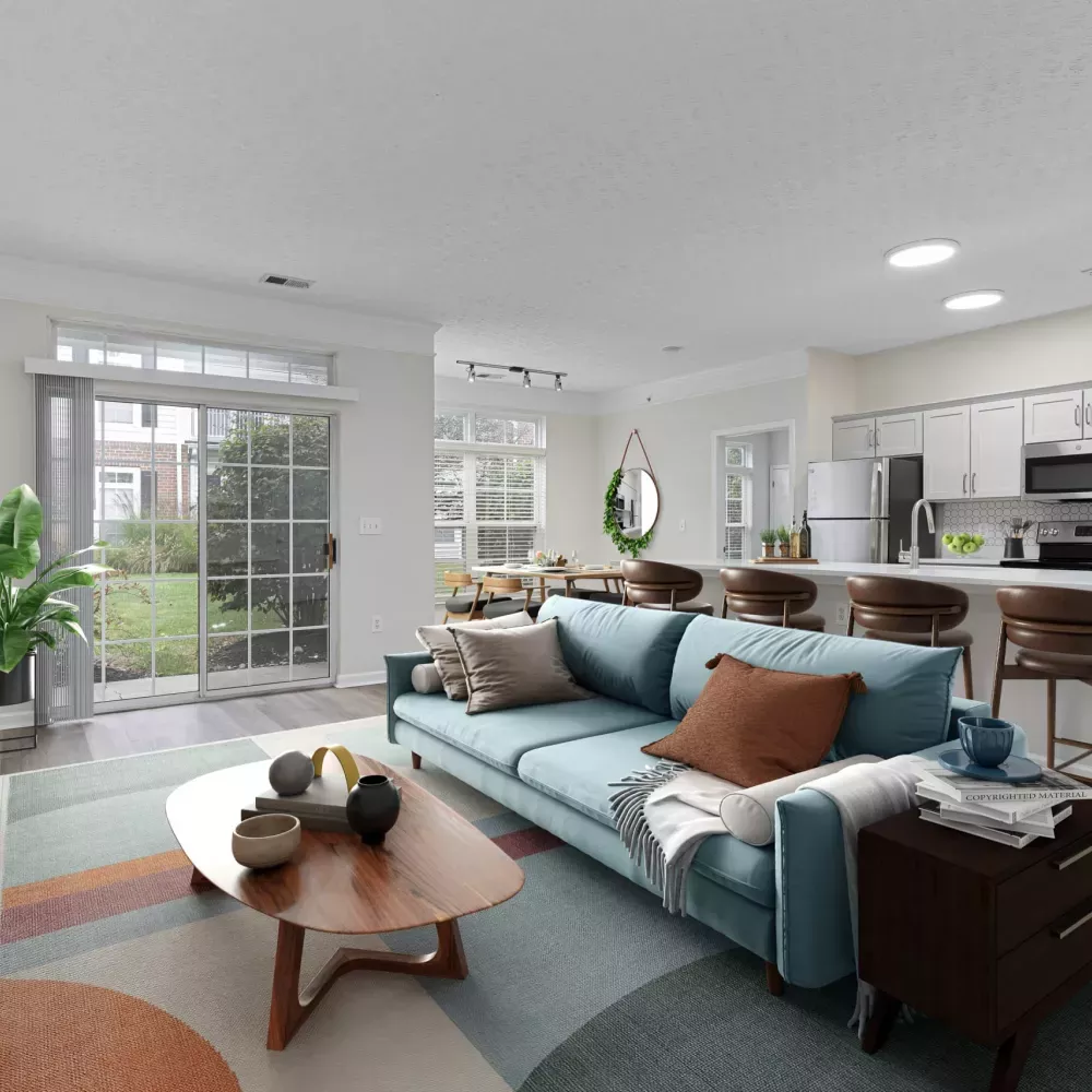 Modern living room with blue sofa, colorful rug, and patio, open to dining area and white kitchen with island bar.
