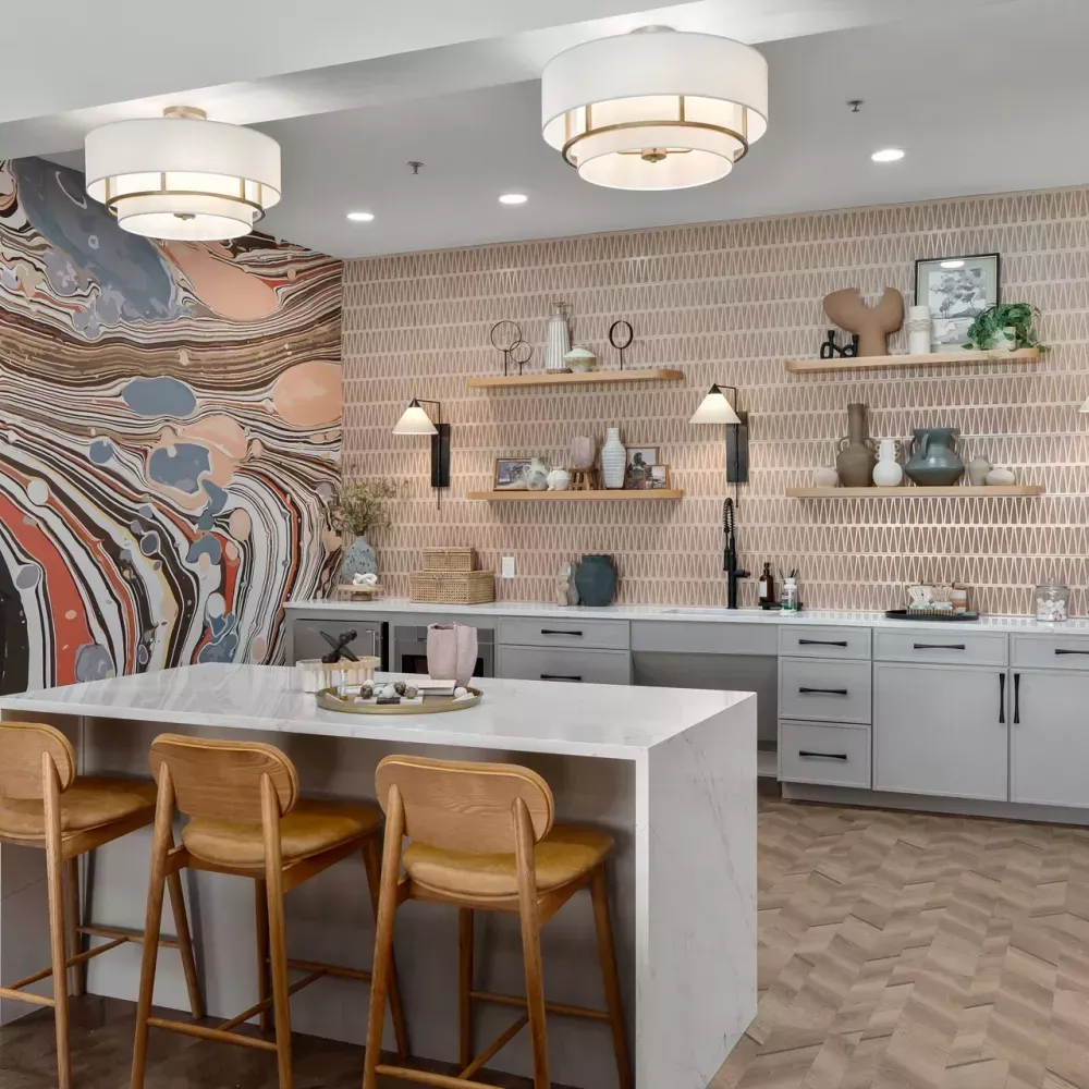 Stylish kitchen area with marble island, brown bar stools, tiled wall, and abstract art in orange, gray, and black.