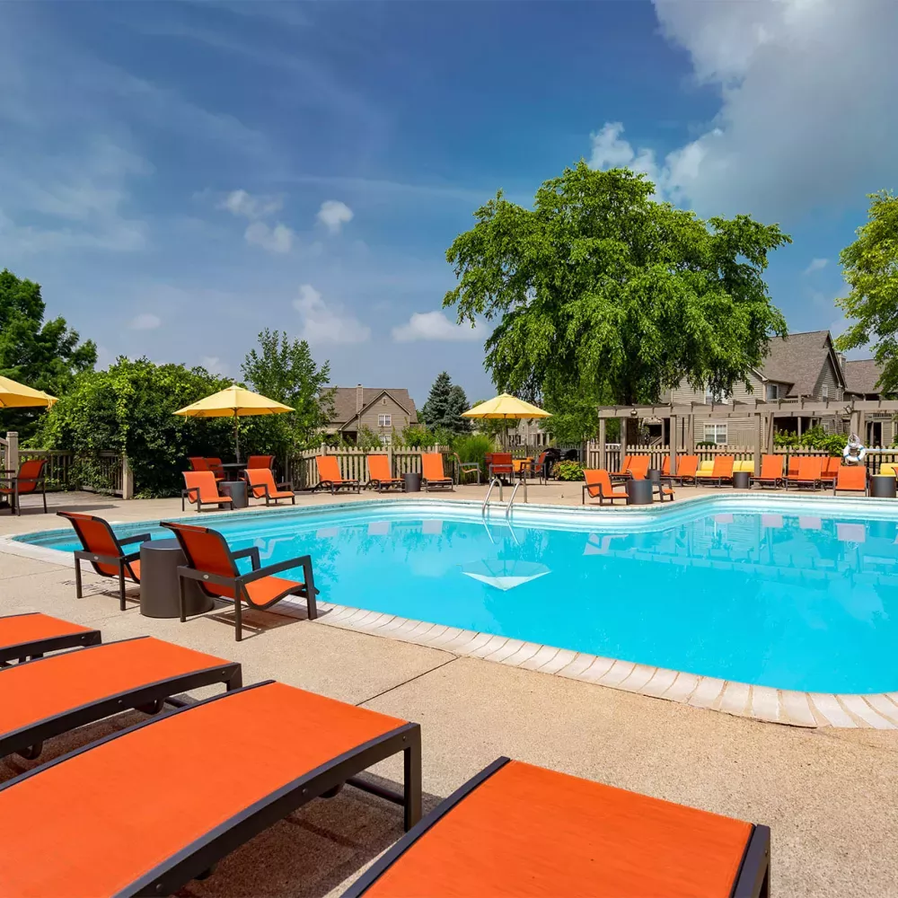 Outdoor swimming pool with orange lounge chairs and yellow umbrellas, surrounded by residential buildings on a sunny day.